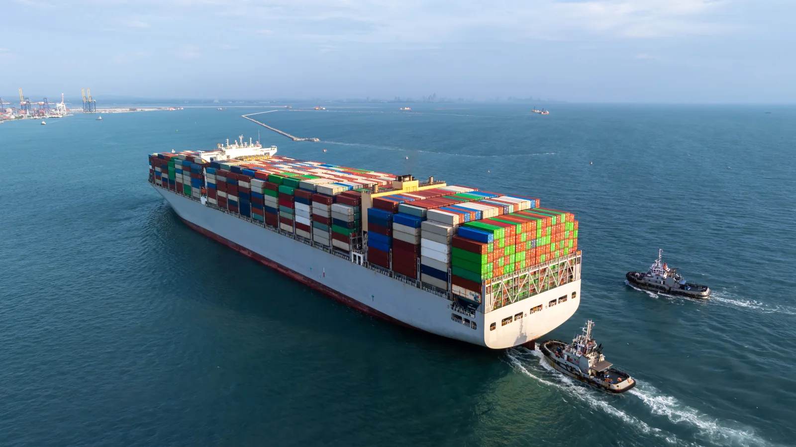 Large container ship assisted by tugboats approaching a major European and Mediterranean container terminal